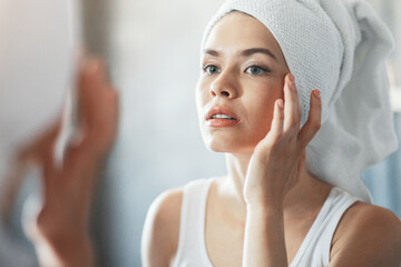 Beautiful millennial woman touching her skin near mirror, checking for wrinkles after shower in bathroom