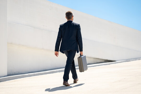 Businessman back walking outdoors. Successful businessman with briefcase in suit. Confident business man back in suit. Business man walking away. Rich man in suit. Urban business man with briefcase. - Powered by Adobe