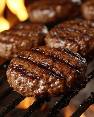 Close-up of four juicy grilled hamburger patties on a barbecue grill with flames in the background.