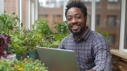 Happy man working on laptop amidst lush indoor plants.