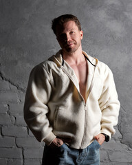 Man in fleece hoodie and jeans, casual pose against wall.