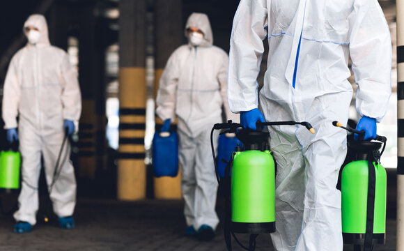 Warning, coronavirus disinfection. Men in virus protective suits carrying spray bottles with chemicals, blurred background