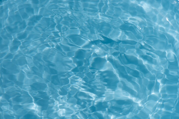 Blue water with ripples on the surface. Defocus blurred transparent blue colored clear calm water surface texture with splashes and bubbles. Water waves with shining pattern texture background.