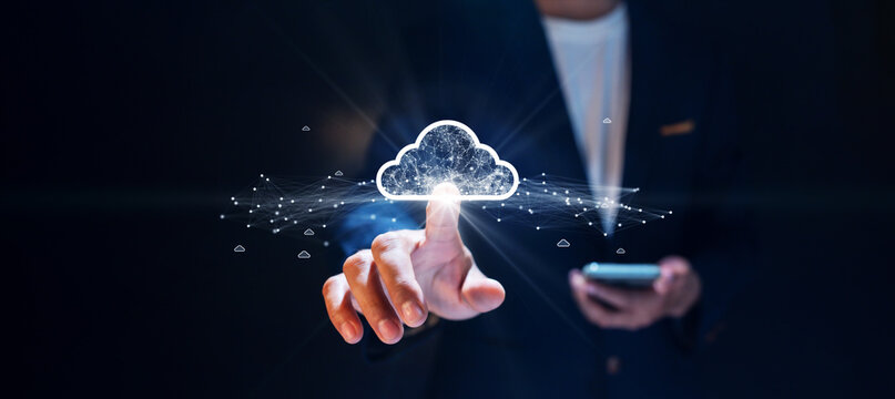 Businessman using smartphone and interacting with glowing digital cloud network, representing cloud computing and data connectivity on dark background.
