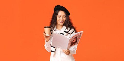 Fototapeta premium Beautiful young Asian woman with magazine and paper cup of hot coffee on orange background