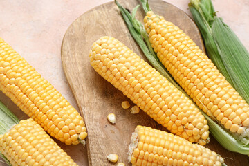 Wooden board with fresh corn cobs on beige table, closeup