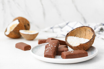 Plate with tasty chocolate covered coconut candies on table