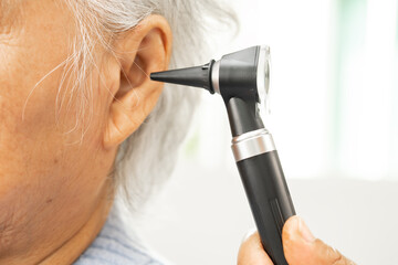 Audiologist or ENT doctor use otoscope checking ear of asian senior woman patient treating hearing loss problem.