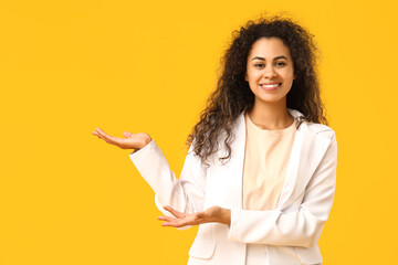 Young African-American businesswoman showing something on yellow background