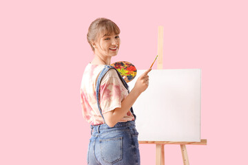 Female artist with paint palette and easel on pink background