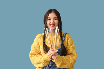Female Asian artist with paint brushes on blue background