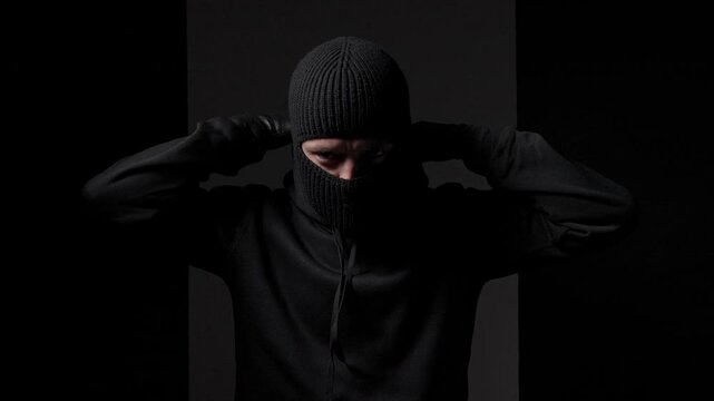 Masked figure adjusting balaclava in shadows