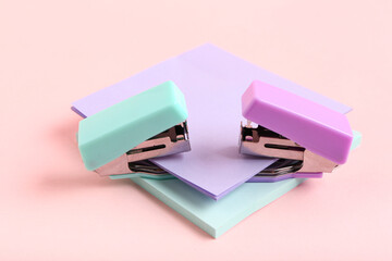 Different small staplers with sticky notes on pink background