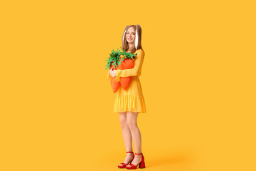 Beautiful woman in bunny ears with toy carrots on yellow background. Easter celebration