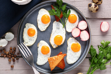Plate with fried quail eggs, toasts and radish on grey wooden table