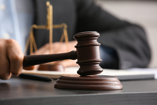 Male judge with gavel and scales of justice at table in courtroom