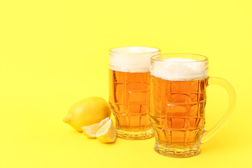 Glasses of fresh beer with lemon on yellow background