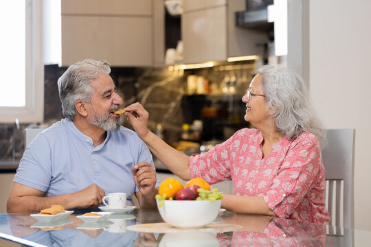 Happy retired senior indian couple eating healthy breakfast together, Romantic elderly husband wife sharing food at table, Love and bonding. Retirement life.