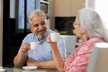 Happy retired senior indian couple enjoy morning eat or coffee together at home, Elderly asian...