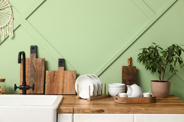 Clean dishes with cutting boards and plant on counter near green wall in kitchen