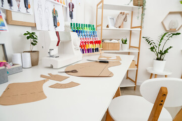 Sewing machine with thread spools and patterns on tailor's table in atelier