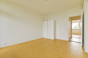 An empty room with a minimalist design, featuring white walls, a simple wardrobe, and a doorway leading to another space, ideal for showcasing interior decor potential.