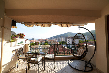 Wicker swing chair stands near a glass table with chairs on a terrace with a canopy
