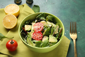 Bowl of tasty avocado salad with cherry tomatoes and lemon on green background