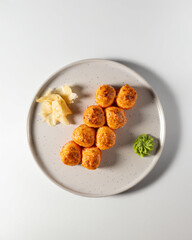 Top-down view of baked sushi rolls with a crispy golden topping, arranged on a white plate with wasabi and pickled ginger. Minimalist food presentation, Japanese cuisine.