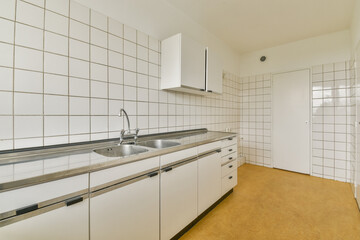 A sleek and minimalistic kitchen showcasing clean lines, tiled walls, and modern fixtures. The design emphasizes functionality and simplicity.