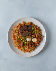 Traditional Uzbek plov pilaf with fragrant rice, tender beef, carrots, and spices, garnished with green onions, quail egg, and garlic. Served on a white plate over a rustic wooden table, top-down view