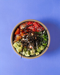 A hand holding a vibrant poke bowl with fresh ingredients, including salmon, avocado, seaweed, and...