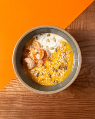 Pumpkin soup with shrimp and cream on a bright accent background and on a wooden table. Vertical...
