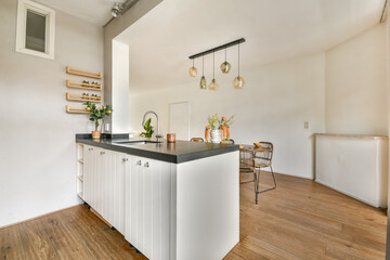 A sleek modern kitchen featuring minimalistic design with white cabinetry, wooden flooring, and stylish lighting fixtures that enhance the atmosphere.