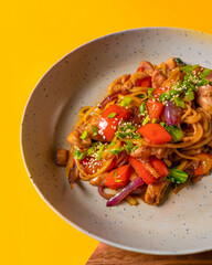 Wok of noodles, vegetables and chicken in soy sauce Chinese food on a yellow background Photo of Chinese food for advertising