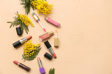 Different lipsticks with lip gloss and mimosa flowers on beige background