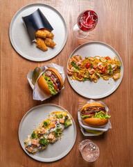 Top-down view of multiple fast-food dishes, including burgers, fries, fish and chips, and various condiments, arranged on a wooden table.