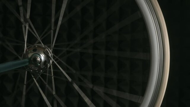 Close-up view of a bicycle wheel rotating against a dark background, showcasing the rhythmic motion of the spokes and the passage of the red valve cap