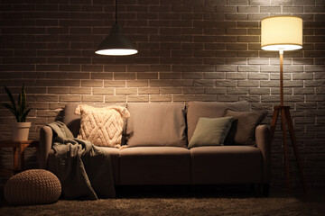 Cozy sofa and glowing lamps in interior of modern living room