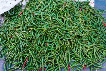 A pile of green chillies are arranged for sale in a market settings 