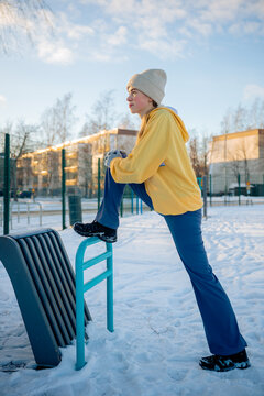 Young woman stretching on outdoor fitness equipment in a snowy park