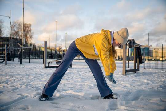 Woman stretching in snowy outdoor gym in winter