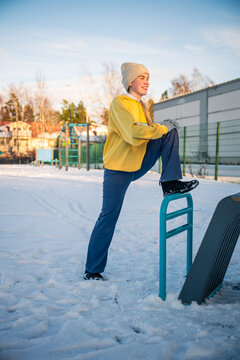 Young woman stretching on outdoor fitness equipment in a snowy park