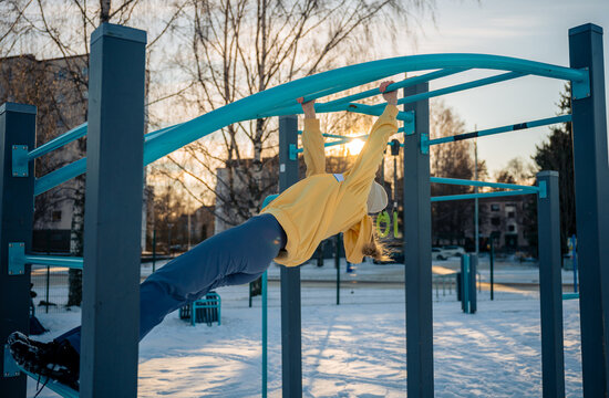 Young woman exercising on monkey bars in winter outdoor gym