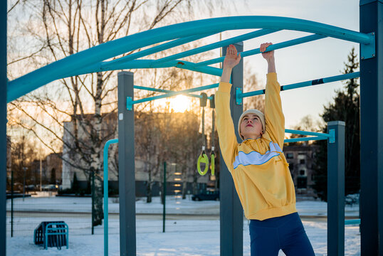 Young woman exercising on monkey bars in winter outdoor gym.