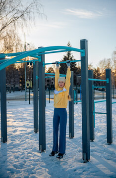 Woman exercising on outdoor gym bars in a snowy park in winter