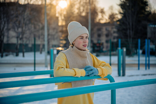 woman in warm winter clothing leaning on blue bars outdoors at sunset