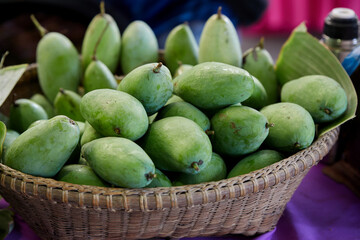 Close-up view of unripe mangoes for sale in bamboo basket
