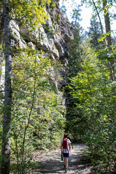 Youthful boy walks on path next to rising rock face in the forest.