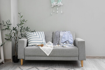 Baby clothes with toys on sofa near light wall in room